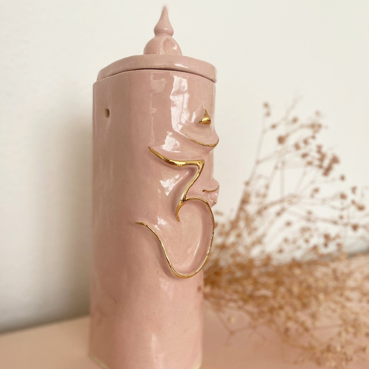 E spirituele herinneringsurn in roze met heilig Om-symbool in gouden reliëf.egante